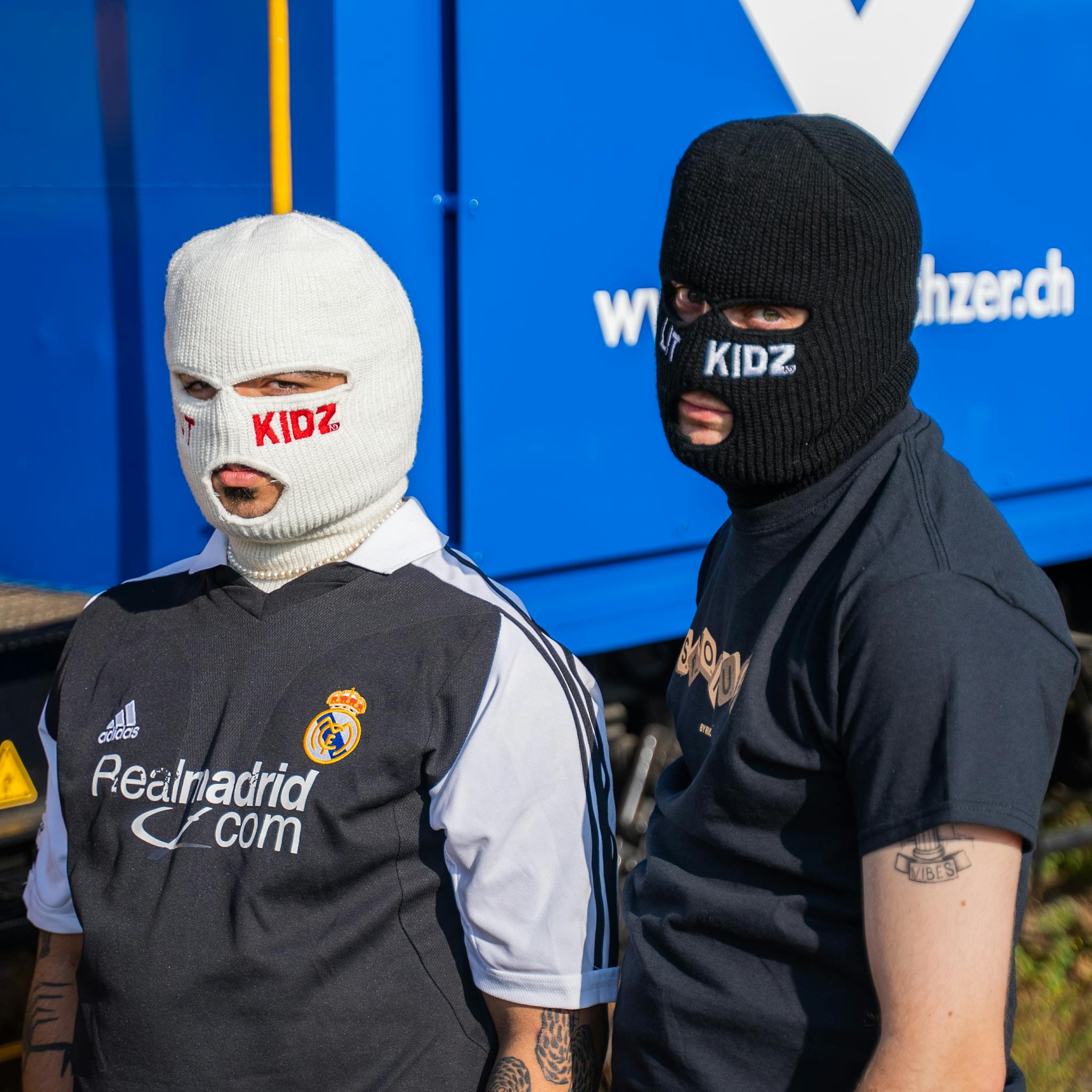 Two adults wearing knit masks and branded apparel in an outdoor setting.